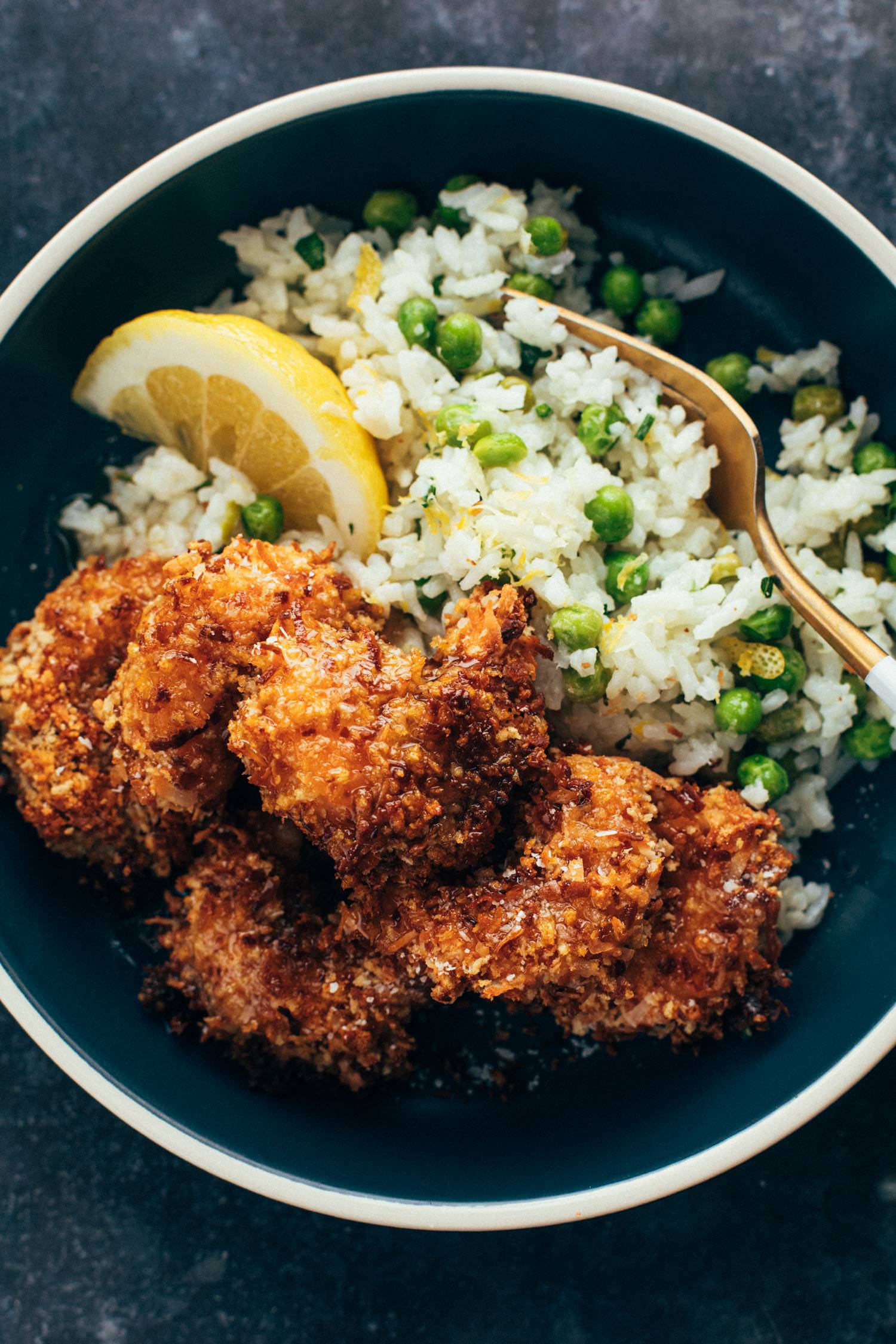 Baked coconut shrimp in a bowl with rice, peas, and a lemon wedge