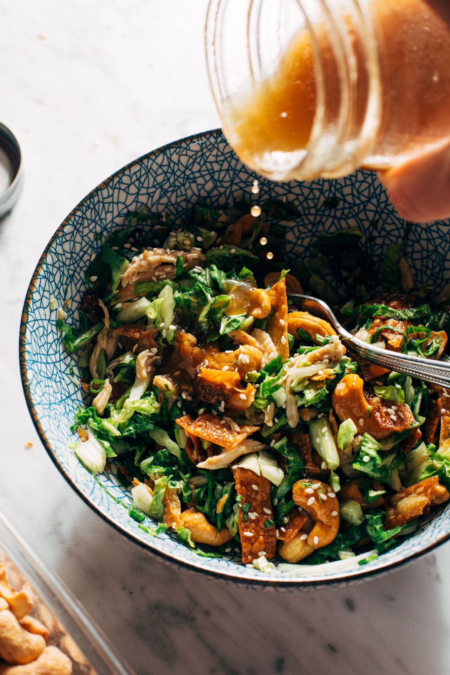 White hand pouring a jar of dressing into a bowl of salad